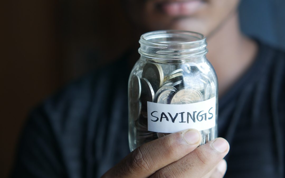 A person holding a jar filled with coins and labelled “Savings”